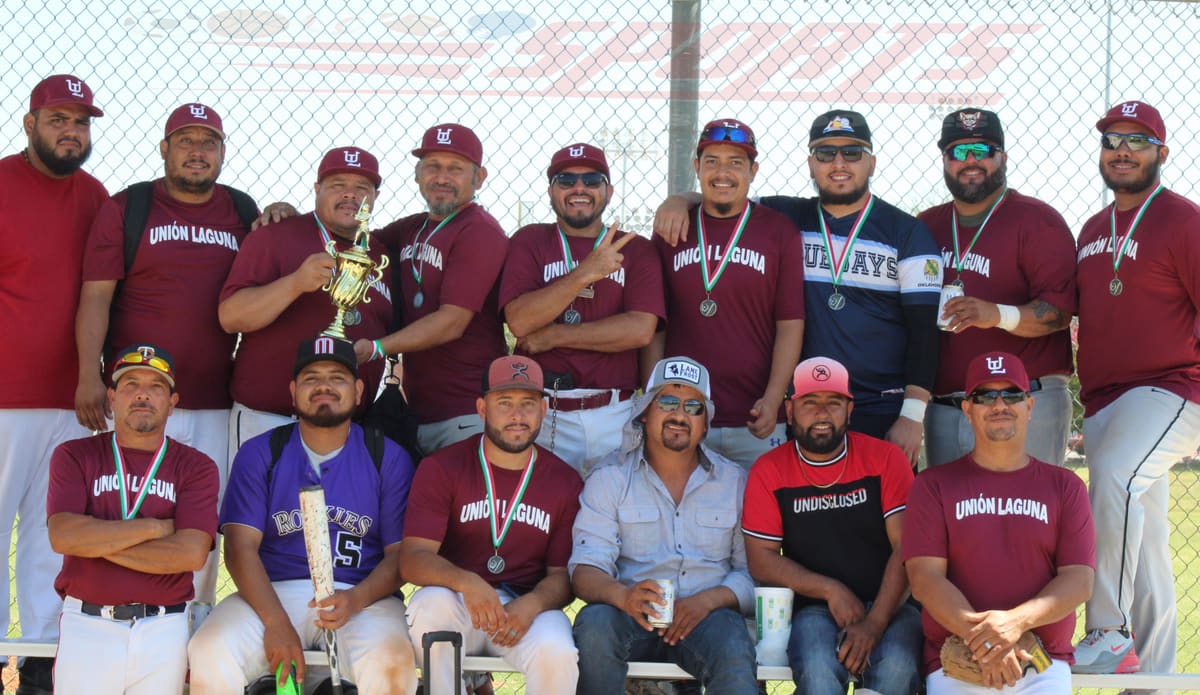 Equipo de béisbol de Unión Laguna posa con medallas y un trofeo dorado frente a la malla del campo, unos de pie y otros sentados en la banca.