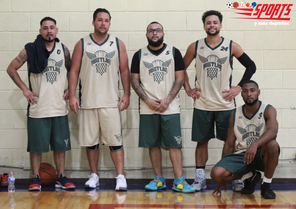 Cinco jugadores de baloncesto con uniforme beige y verde posan recargados en la pared de un gimnasio, con el balón a sus pies.