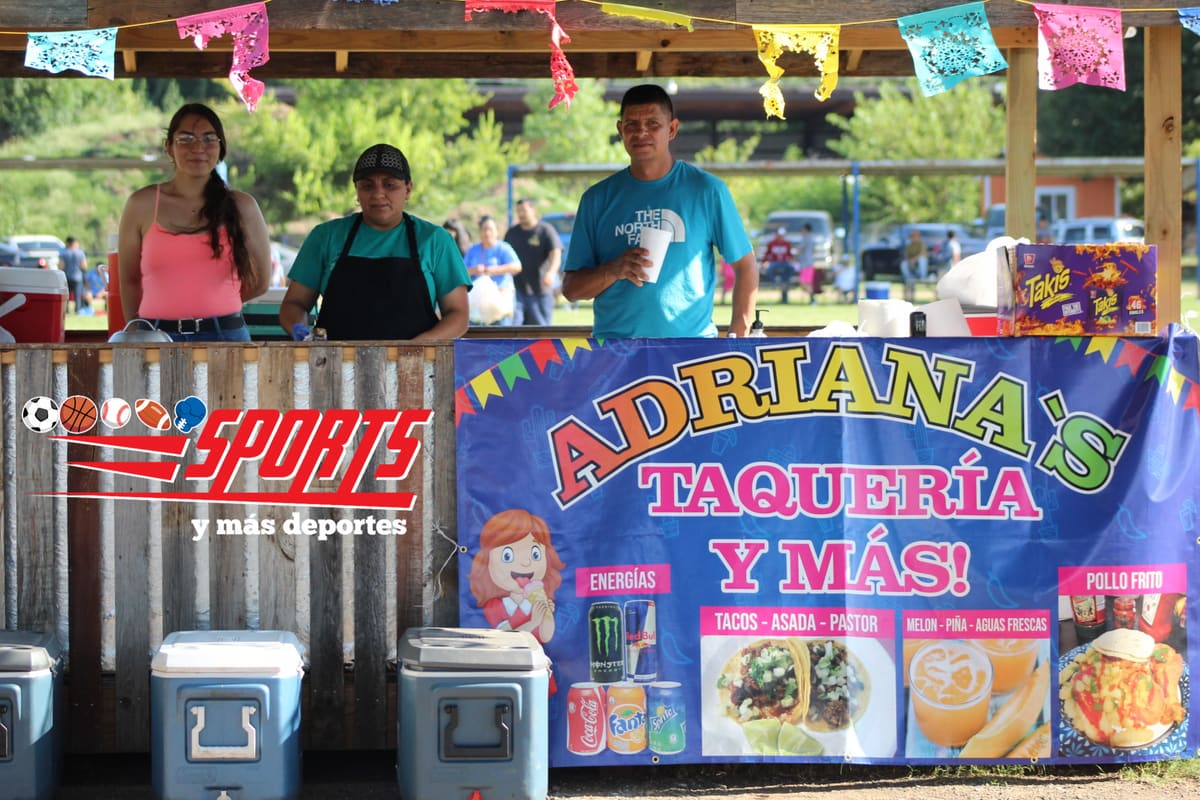 Dos mujeres y un hombre atienden un puesto de tacos en el parque, detrás de una lona de colores y varias hieleras, con papel picado colgado del techo.