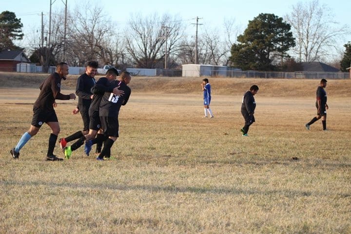 Jugadores de negro se abrazan festejando en el campo mientras los rivales de azul se alejan cabizbajos.